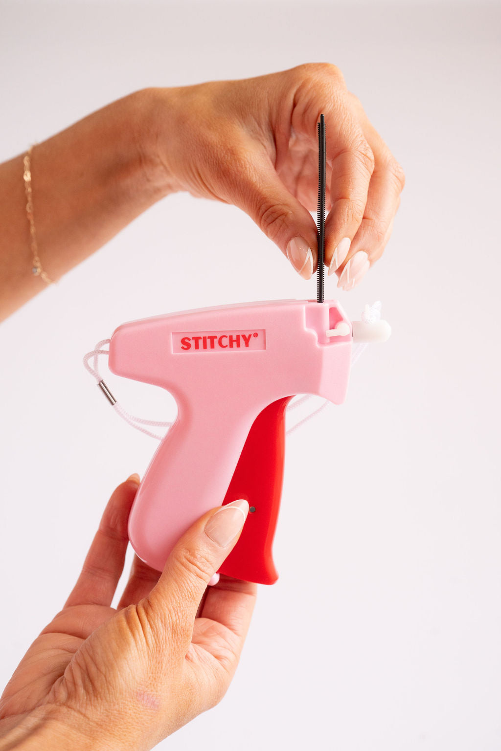 Tucky Stitchy Quick Fix Clothing Gun held in hand for easy clothing alterations, featuring a pink and red design.